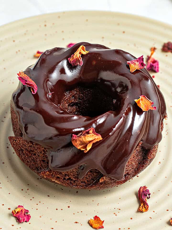 Rose petals sprinkled on chocolate glazed mini bundt cake. Greenish plate.