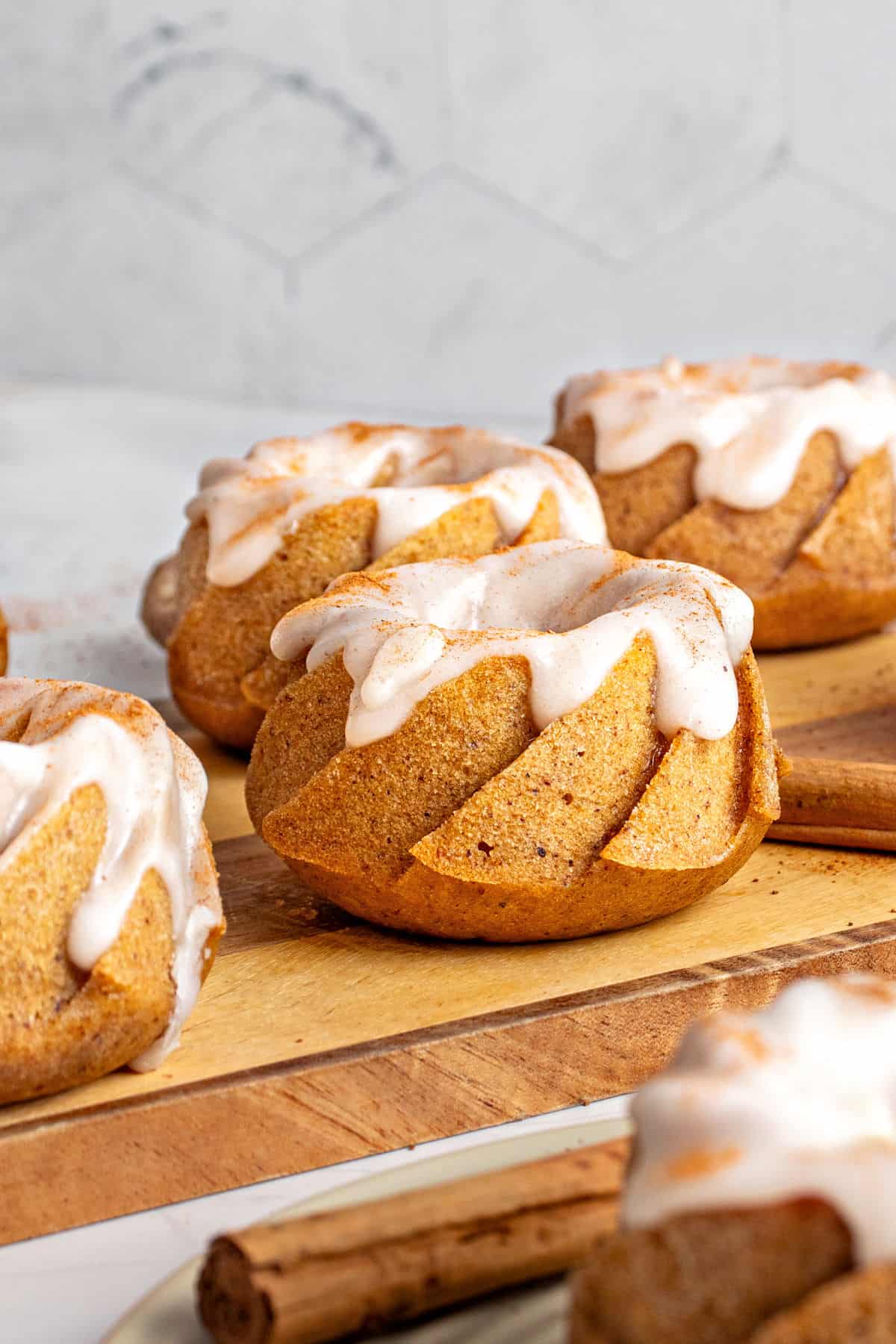 Several glazed mini pumpkin bundt cakes on a wooden board. Gray background. 