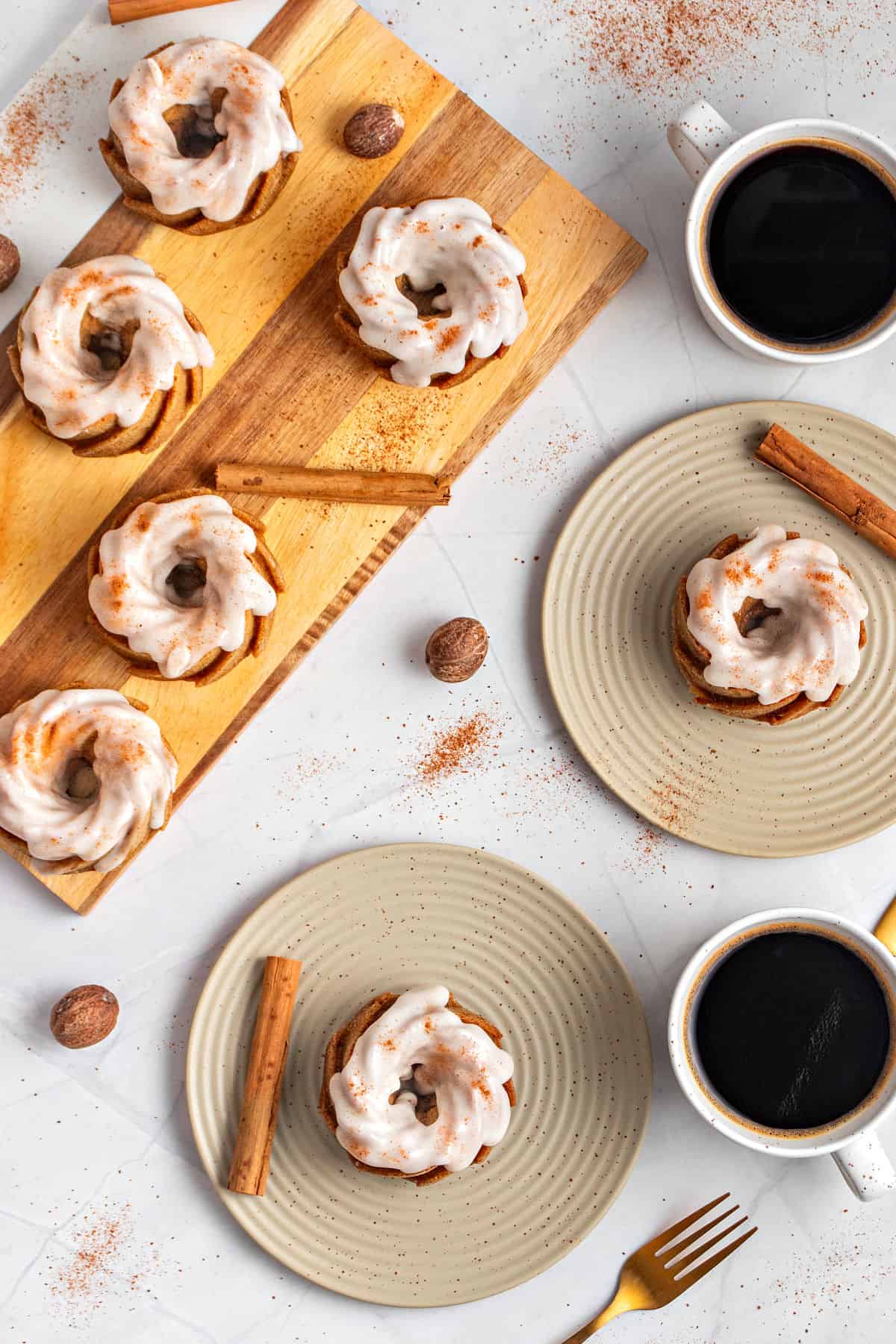 Top view of wooden board and dry green plates with glazed mini bundt cakes. Gray surface, coffee cups.