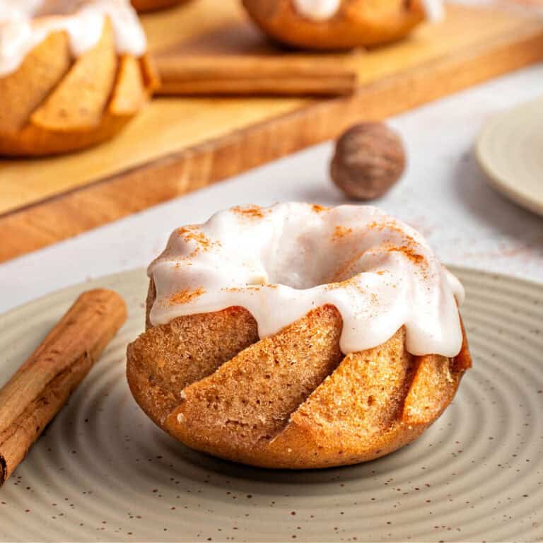 Dry green plate with single glazed mini pumpkin bundt cake. Wooden board, cinnamon sticks.