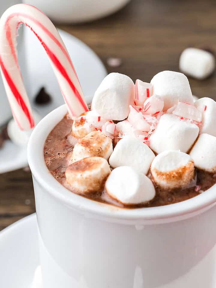 Marshmallow candy cane topped hot chocolate in a white cup. Wooden surface.