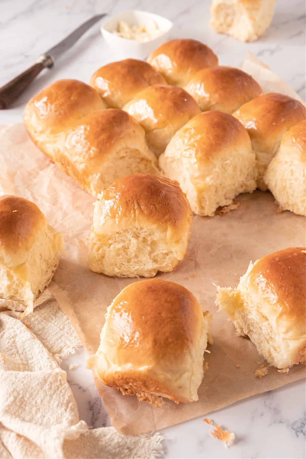 Several dinner rolls on beige paper. White marble surface, a knife, kitchen towel.