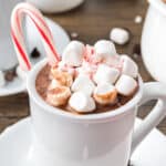 Marshmallow candy cane topped hot chocolate in a white cup. Wooden surface.