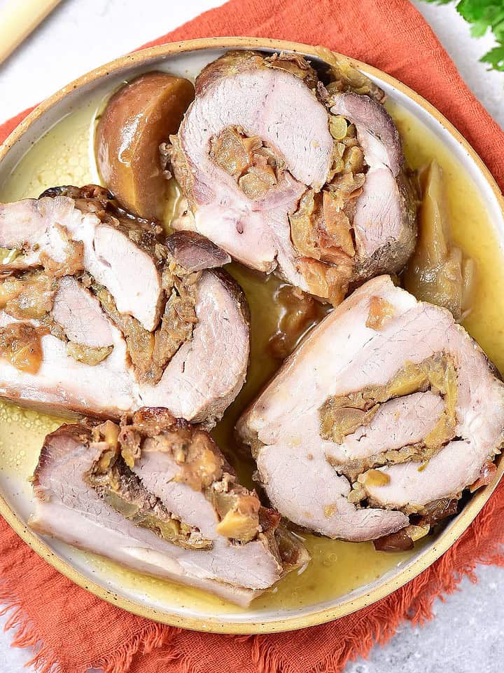 Several slices of apple-stuffed pork roast on a yellowish plate over an orange napkin.