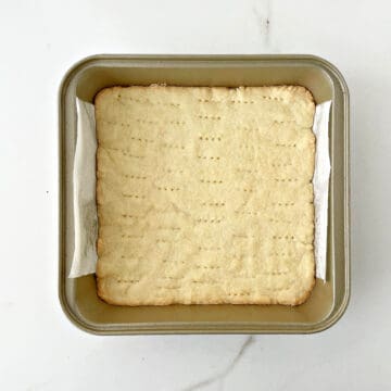 Blind baked shortbread crust on golden square metal pan. Top view.