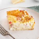 Serving of ham and cheese bread pudding on a light pink plate. Siver fork.