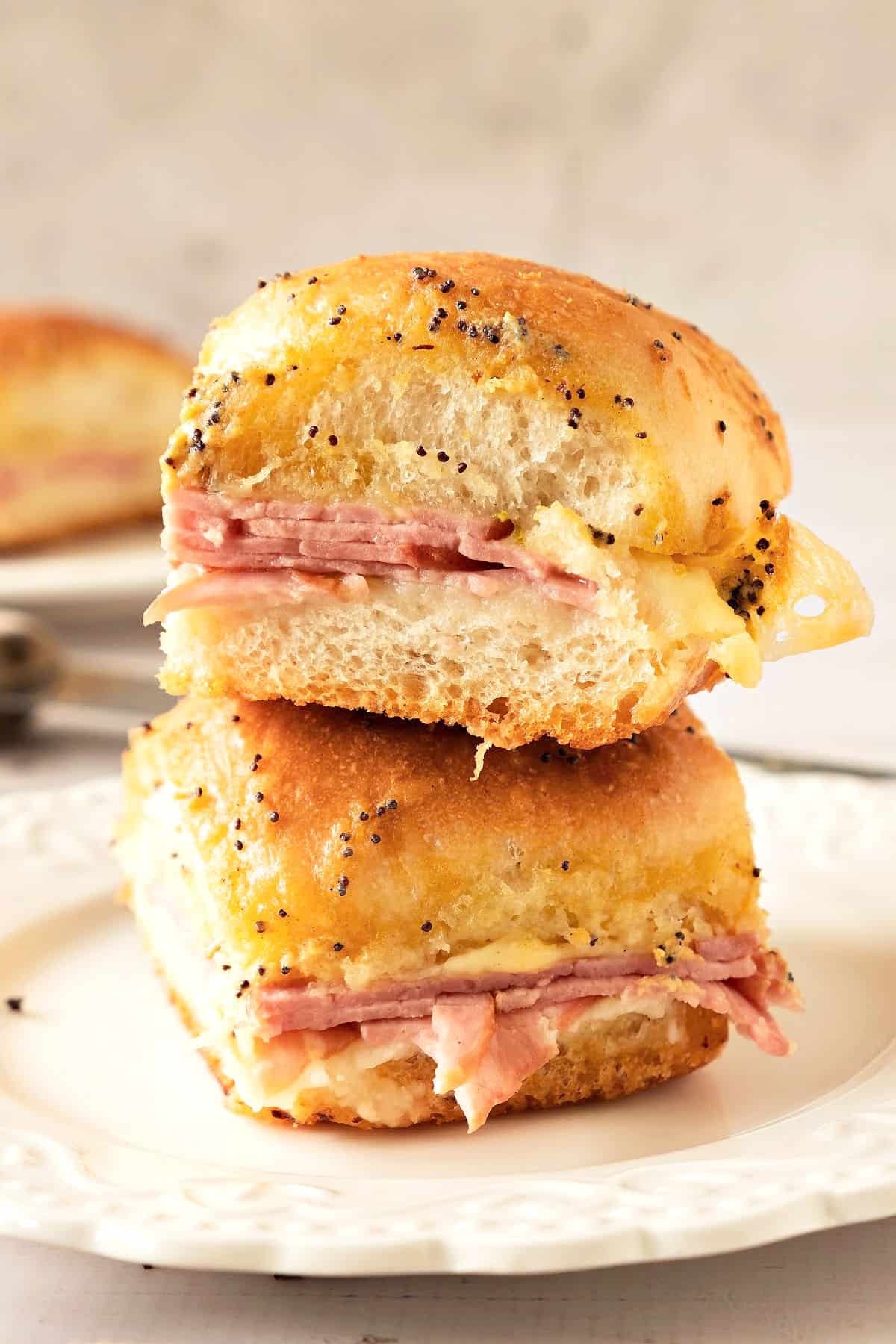 Two ham and cheese sliders stacked on a white plate. Gray background.