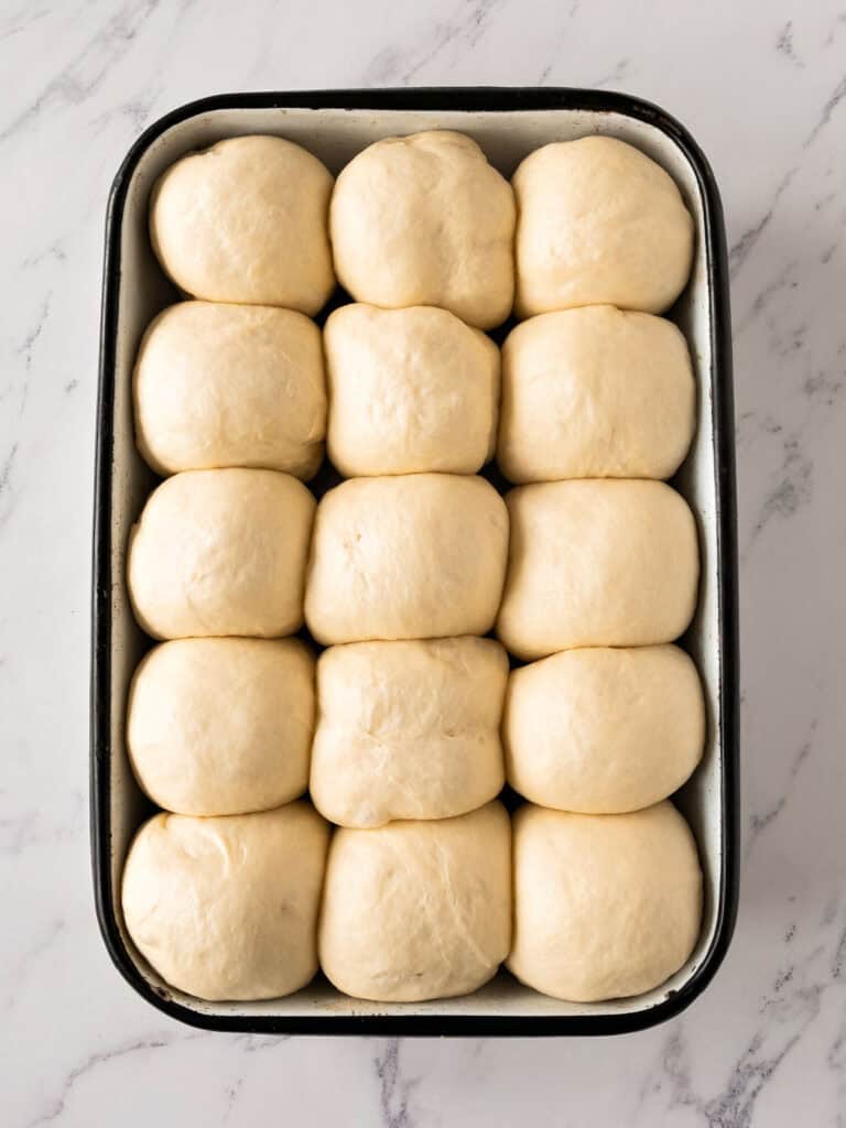 Proofed rolls in a rectangular enameled pan. White marbled surface. Top view.