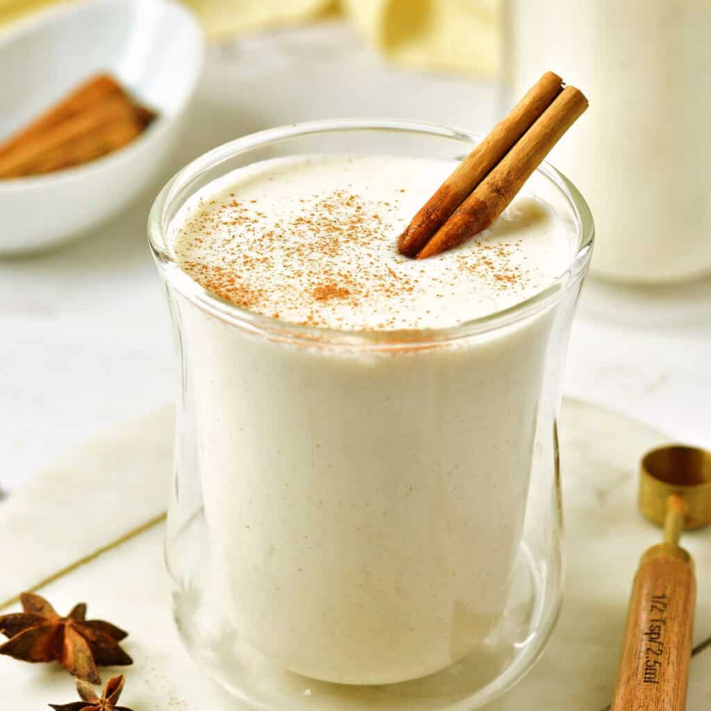 Glass of eggnog with cinnamon stick on a white board. Wooden spoon, anise stars.