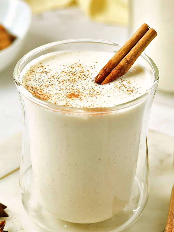 Glass of eggnog with cinnamon stick on a white board. Wooden spoon, anise stars.