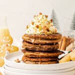 Stack of gingerbread pancakes with whipped cream and syrup on white plate. Christmas decorations, white background.