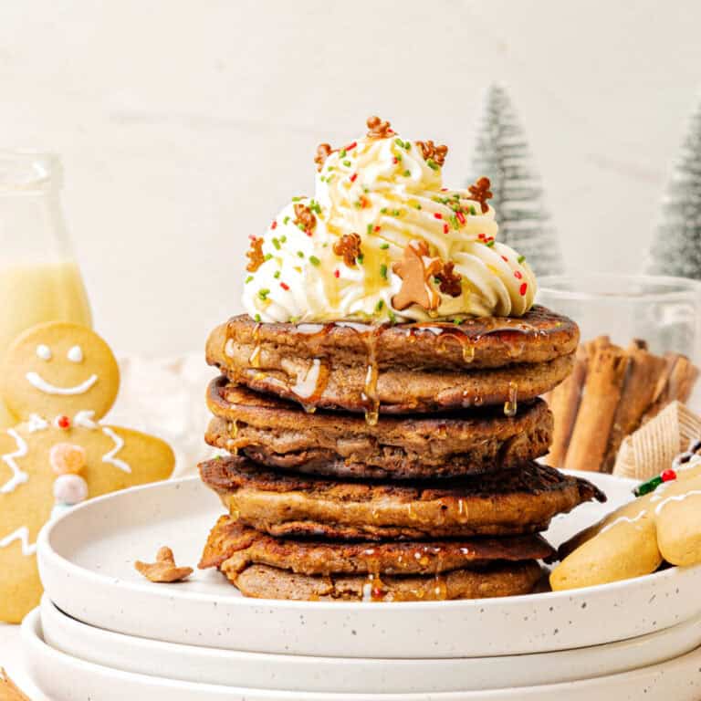 Stack of gingerbread pancakes with whipped cream and syrup on white plate. Christmas decorations, white background.