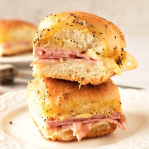 Close up of two ham and cheese sliders stacked on a white plate. Gray background.