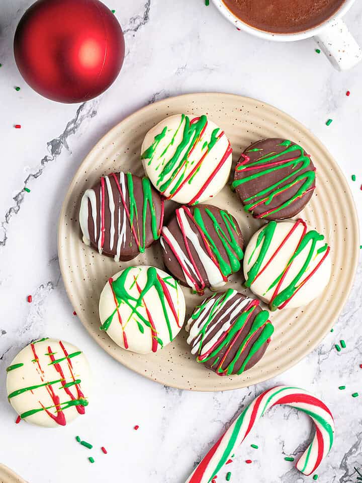 Top view of beige plate with Christmas chocolate covered cookies. Marble surface, sprinkles, candy canes.