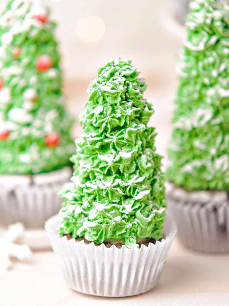 White paper liners with Christmas tree cupcakes decorated with green buttercream. White background.