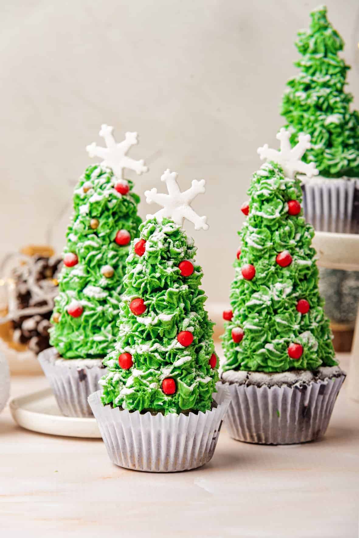 Several white paper liners with Christmas tree decorated cupcakes. Light gray background.