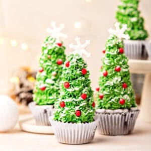 Christmas tree cupcakes in white paper liners. Beige background. Festive decorations.