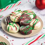 Pile of festive chocolate covered Oreos on a beige plate. White marble surface, sprinkles and candy canes.