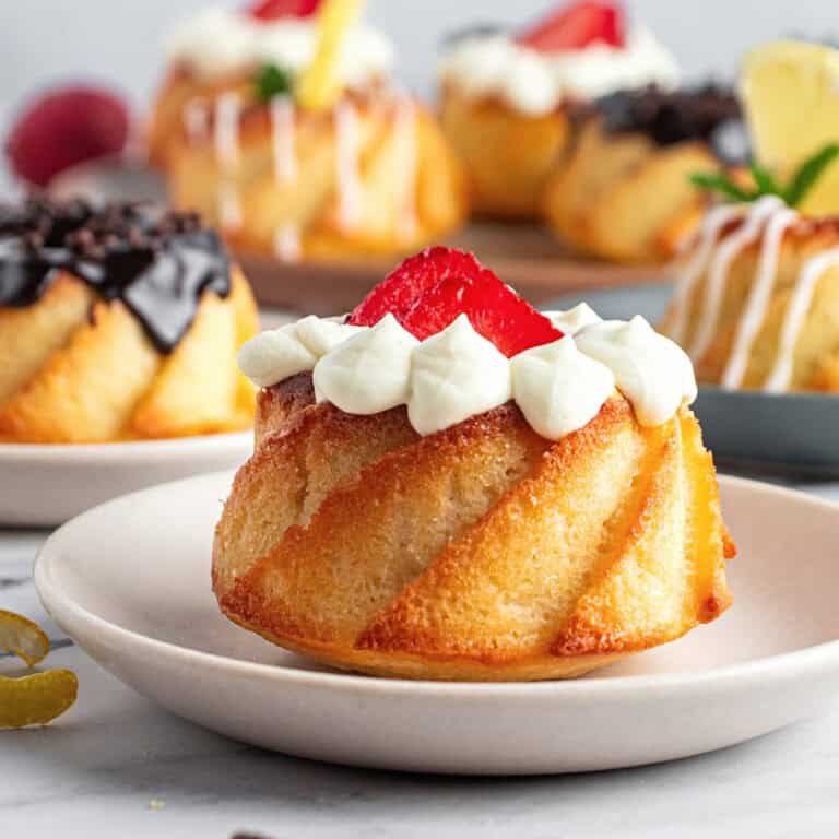 White plate with mini bundt cake with strawberries and cream. More bundts in the background. 
