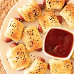 Close up of white platter with pigs in a blanket and bowl of ketchup.