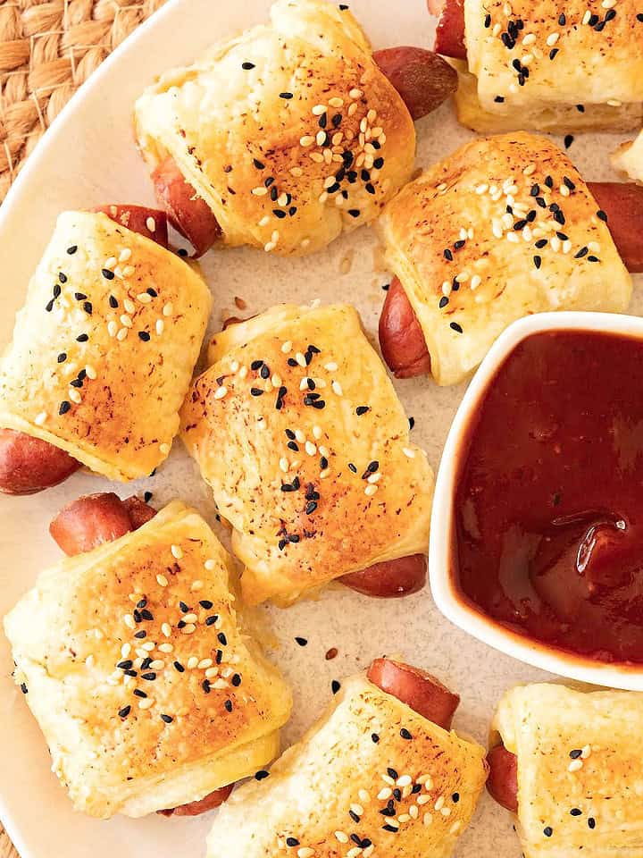 Close up of white platter with pigs in a blanket and bowl of ketchup.