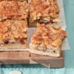 Several raspberry jam almond shortbread bars on a wooden board. Light blue cloth.