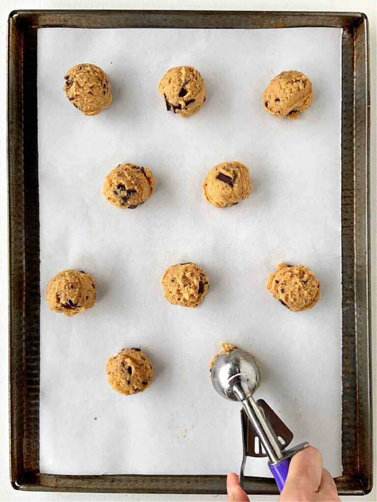 Scooping cookie dough balls on parchment-lined cookie sheet. Top view.