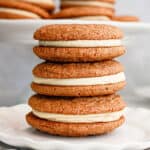 Gray background with stack of gingerbread sandwich cookies on a white plate.