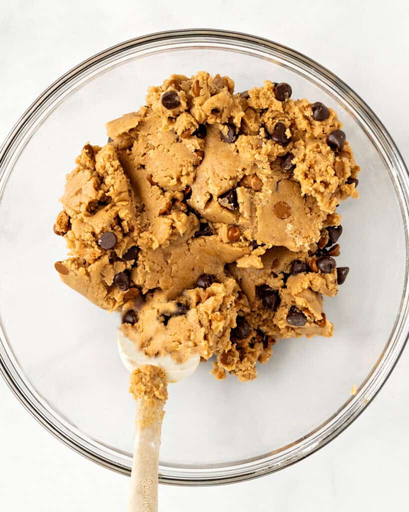 Glass bowl with cookie dough with chips. A spatula. Top view. White background.