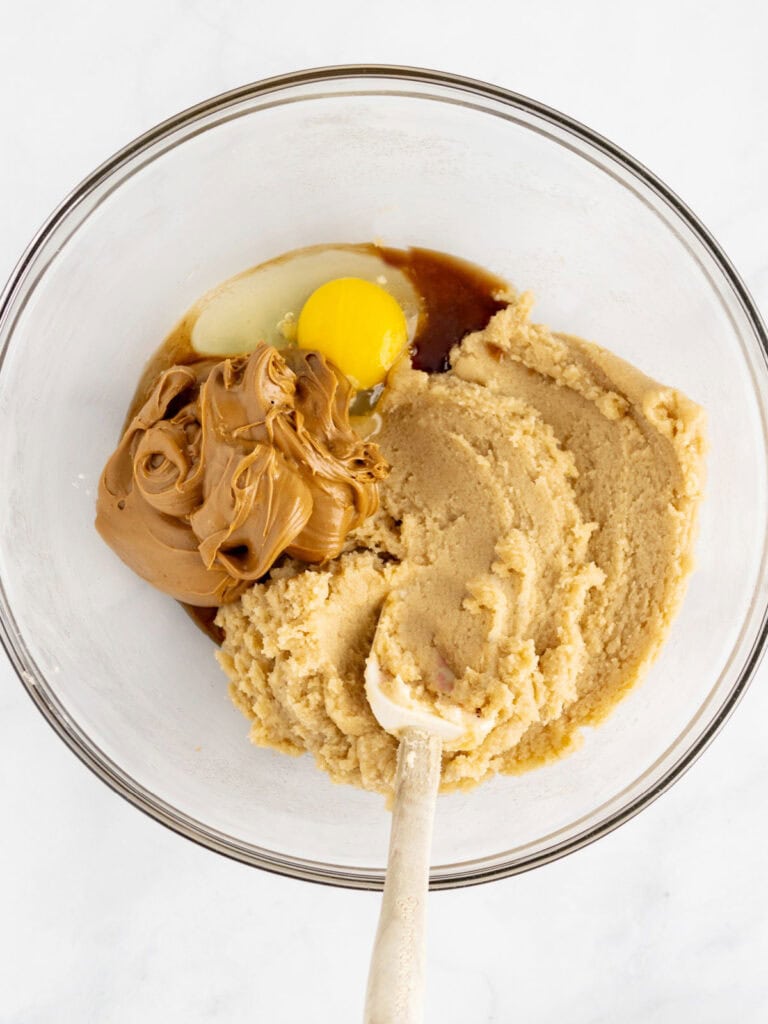 Top view of glass bowl with cookie dough ingredients. A spatula. White background.