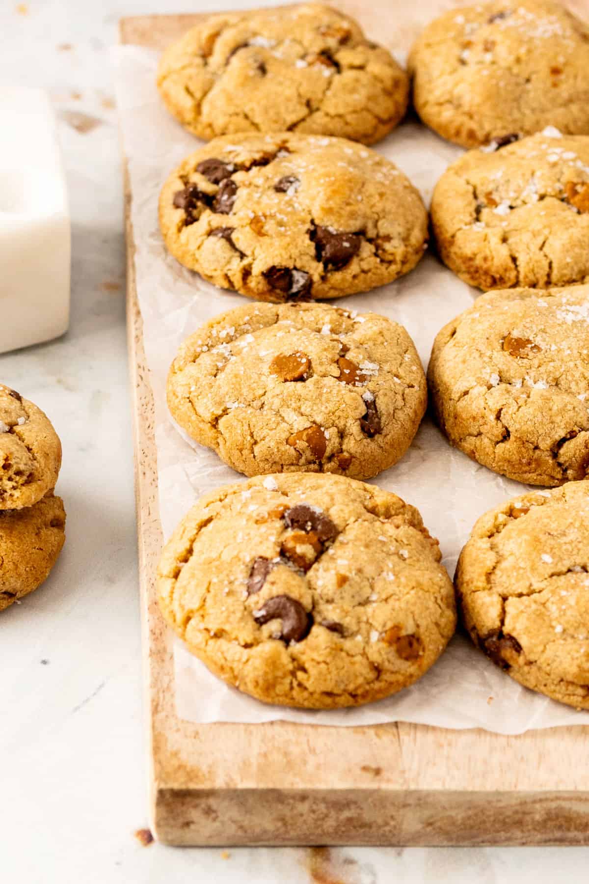 Wooden board with parchment paper and rows of cookies with chips.