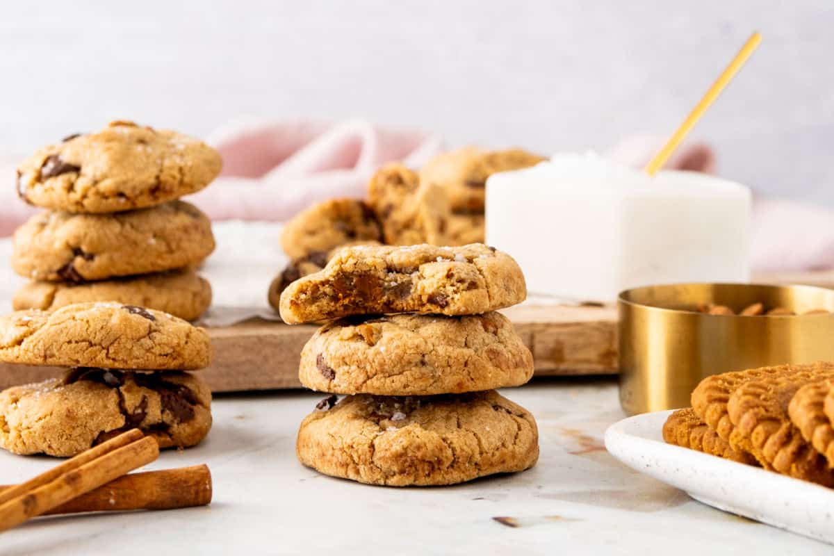 Stacks of Biscoff chip cookies on a white surface and wooden board. Light gray background.