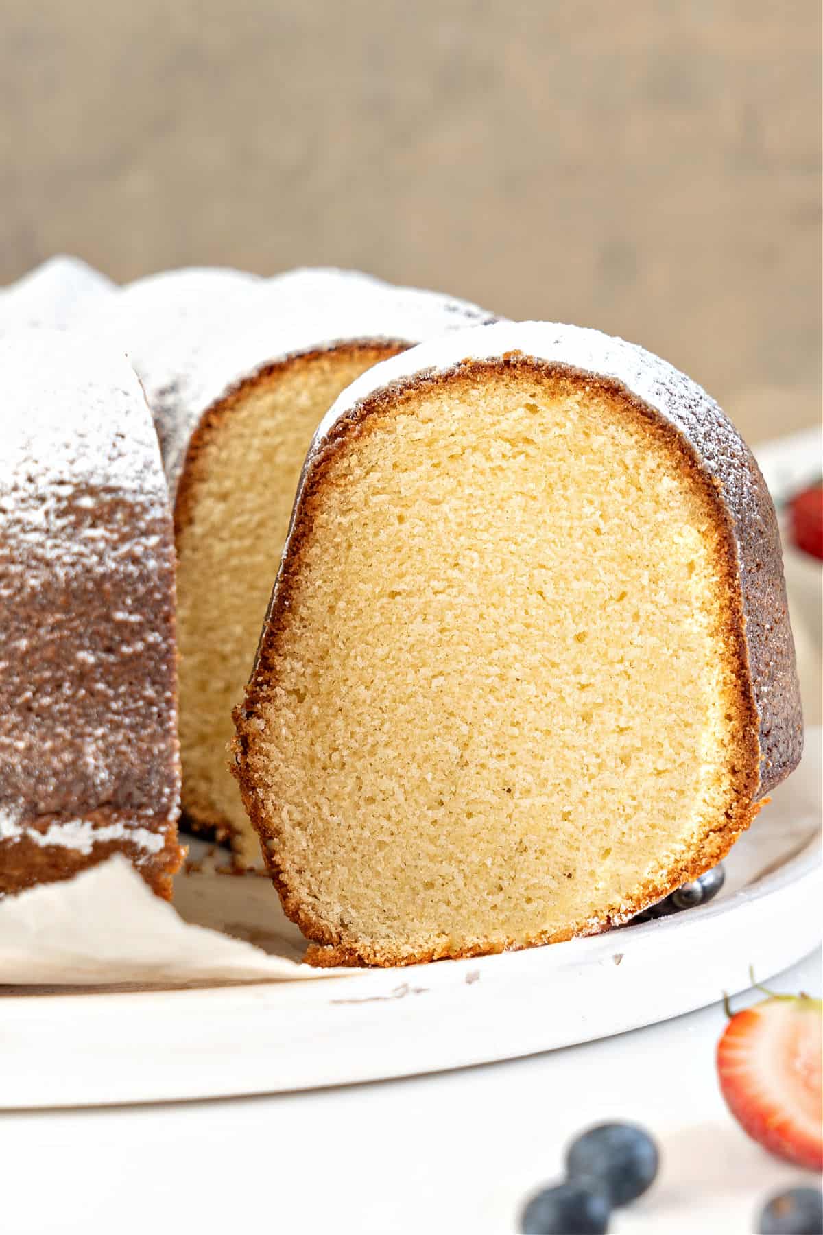 Close up sliced and whole vanilla bundt cake on a white plate. Brownish background.