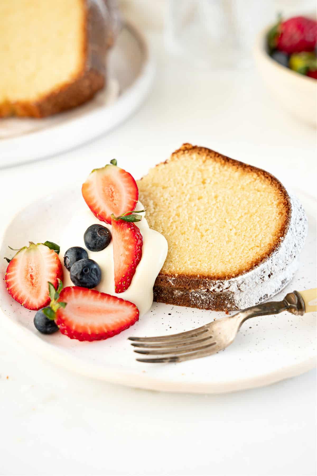 Serving of bundt cake with cream and berries on a white plate. White background.