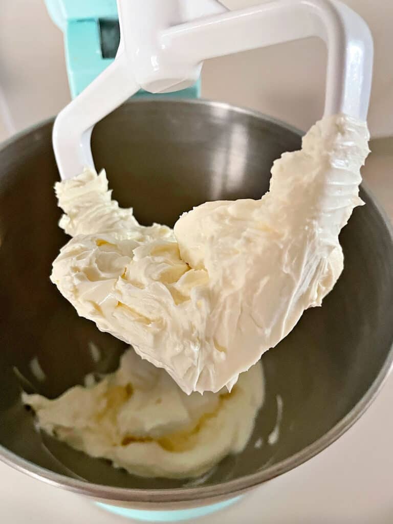 Stand mixer paddle with cream cheese and butter mixture. Metal bowl.