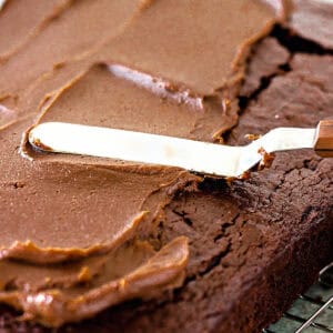 Offset spatula spreading chocolate and peanut butter frosting on a rectangular chocolate cake.