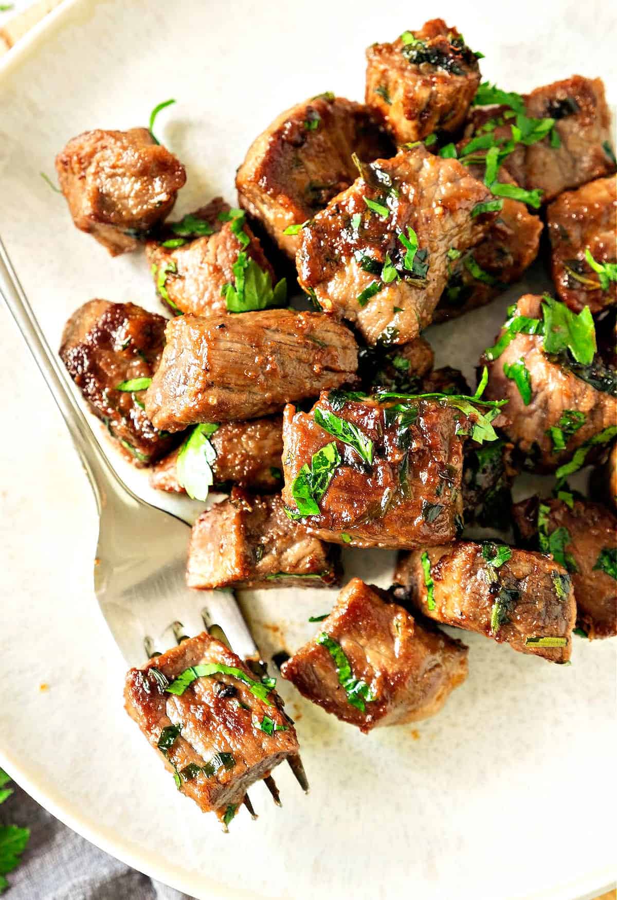 Steak biter with parsley on a white plate. Silver fork. 