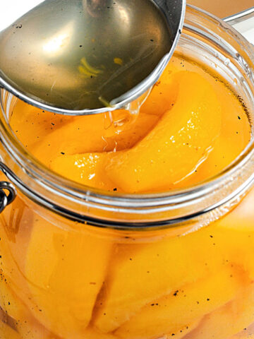 Syrup poured from a silver spoon into a mason jar with peach slices.