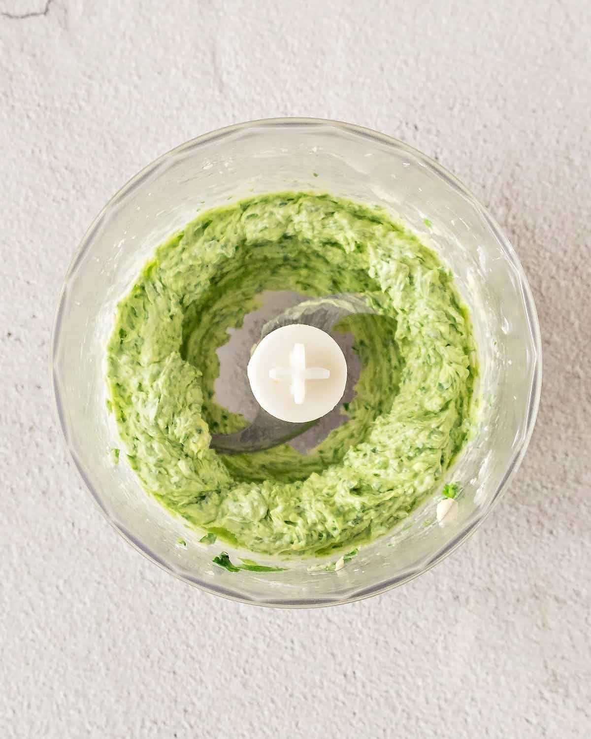 Food processor jar with herb butter. Gray surface. Top view.