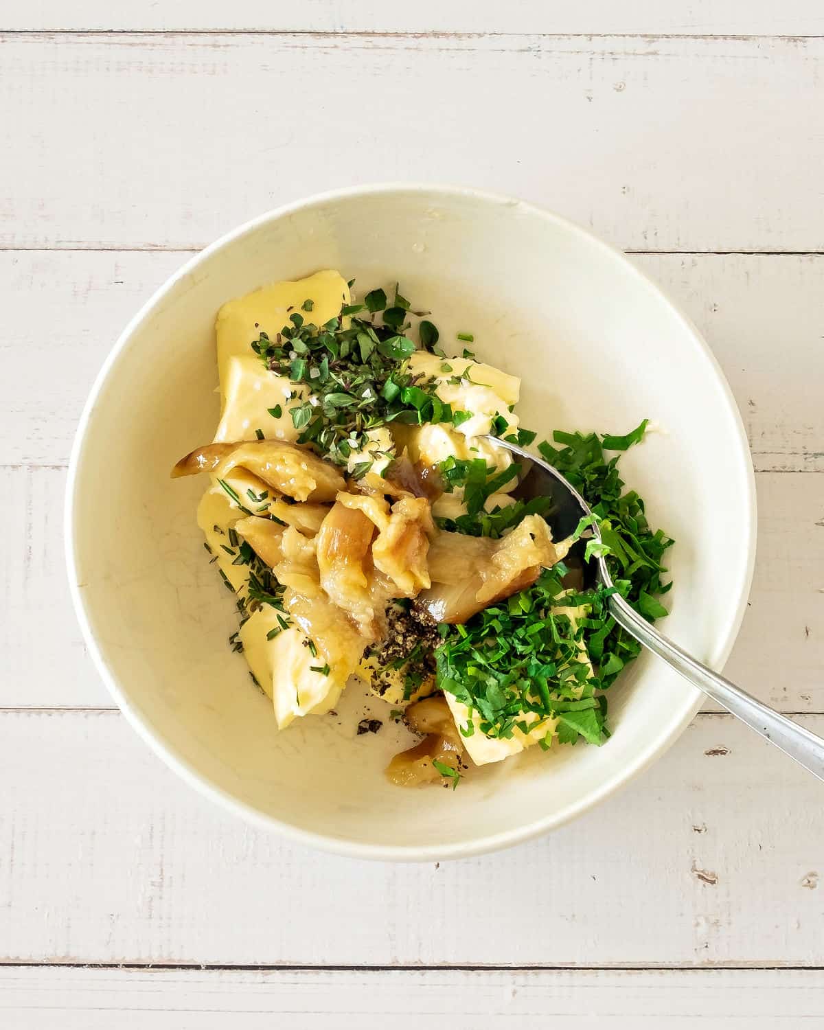 Roasted garlic, parsley and butter in a white bowl. Silver spoon. White background.