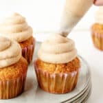 Piping cinnamon cream cheese frosting on cupacakes. Gray plate, white background.