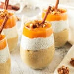 Glasses with chia pumpkin pudding, walnuts and cinnamon sticks. Whitish background.