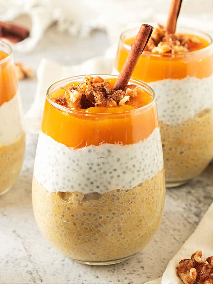 Glasses with chia pumpkin pudding, walnuts and cinnamon sticks. Whitish background.