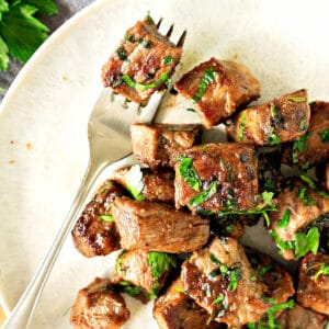 Close up steak bites with parsley on a white plate. Silver fork.