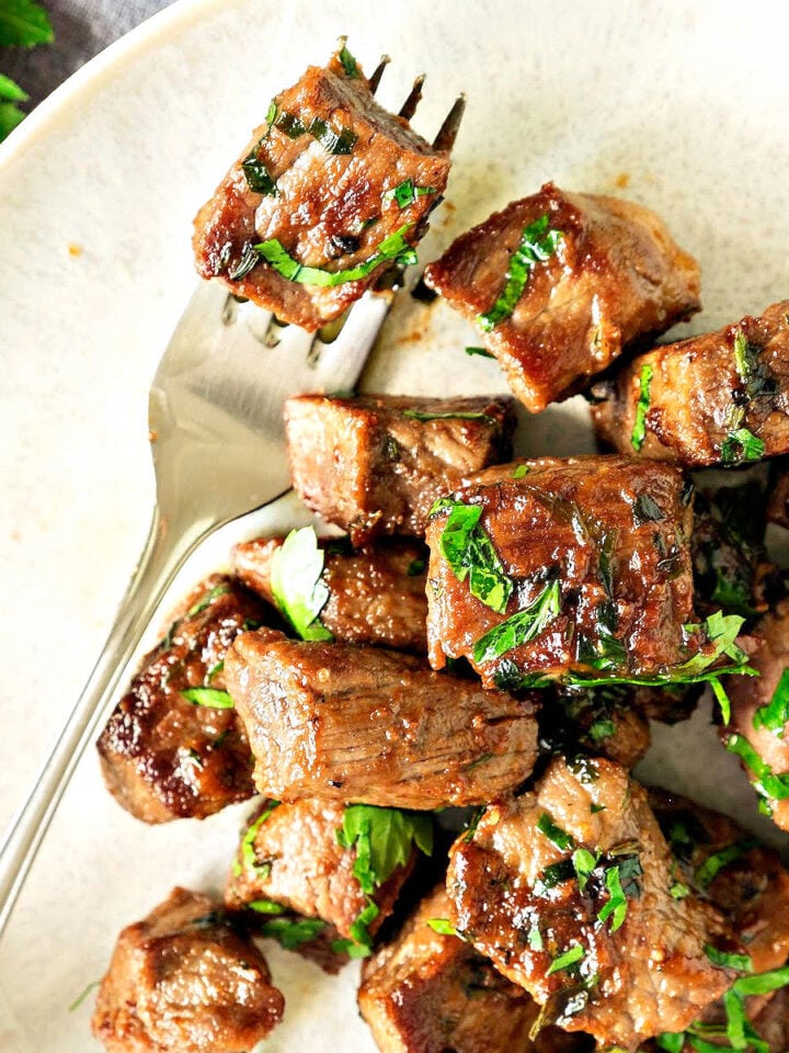 Close up steak bites with parsley on a white plate. Silver fork.