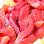 Red, white and black text overlay on pile of beet gravlax pieces with lemon wedges.