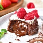 Molten center chocolate lava cake with fresh raspberries. White plate, powdered sugar dusting.