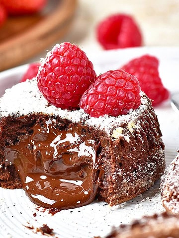 Molten center chocolate lava cake with fresh raspberries. White plate, powdered sugar dusting.