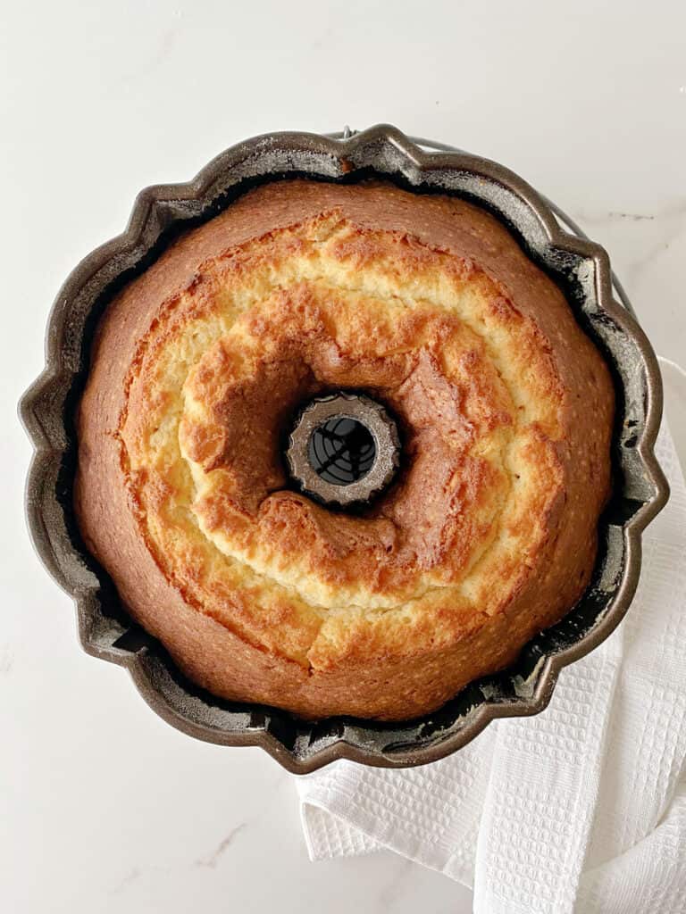 Plain bundt cake in the dark pan. White kitchen towel and surface. Top view.