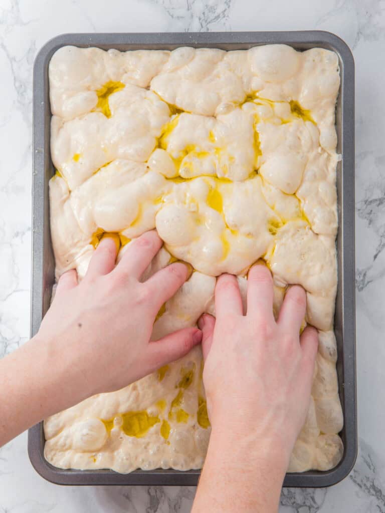 Dimpling focaccia dough with oil in a rectangular baking pan. Top view.